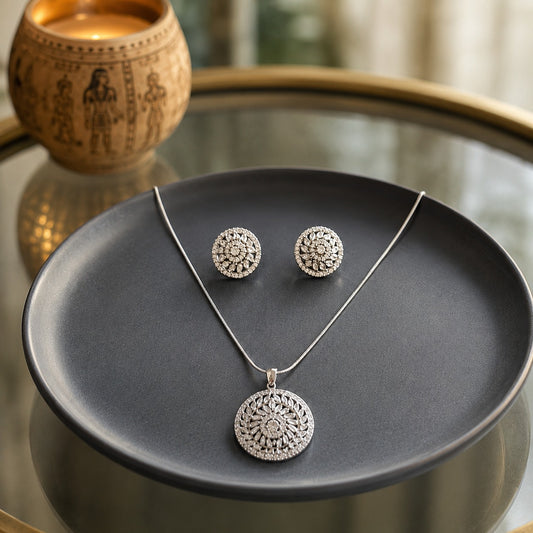 Silver floral pendant and matching stud earrings jewellery set with crystal clear centre stones displayed on a premium charcoal ceramic plate in a luxury lifestyle setting.