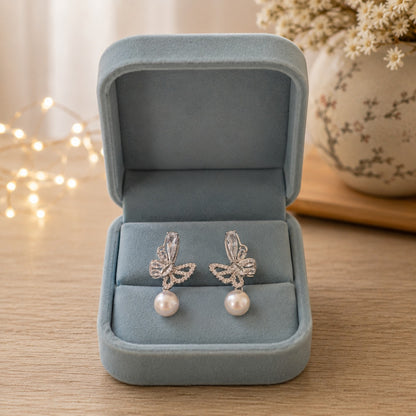 Silver butterfly pearl drop earrings featuring marquise-cut crystals, pavé detailing, and luminous pearl drops displayed inside a premium powder blue velvet jewellery box