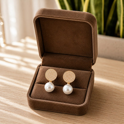 Gold pavé pearl drop earrings featuring round crystal-studded tops and luminous white pearl drops displayed inside a premium chocolate brown velvet jewellery box