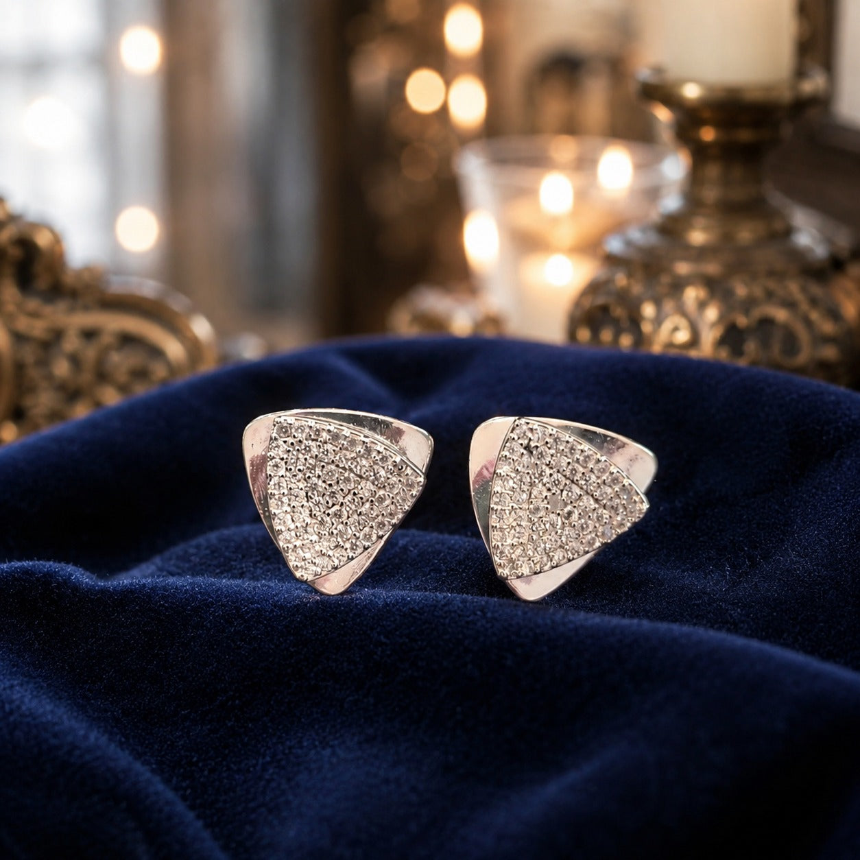 Silver geometric triangular stud earrings with pavé-set crystals displayed on luxurious navy blue velvet fabric in a premium jewellery presentation.