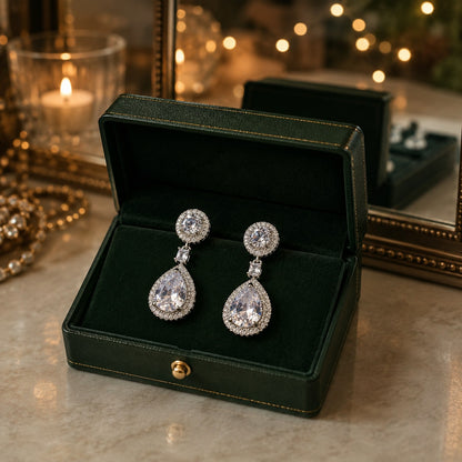 Silver drop earrings featuring a round crystal stud, princess-cut connector, and pear-shaped crystal drop displayed in a premium dark green jewellery box.