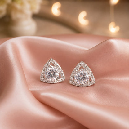 Triangular silver crystal stud earrings with a round-cut centre stone and pavé halo displayed on soft satin fabric.