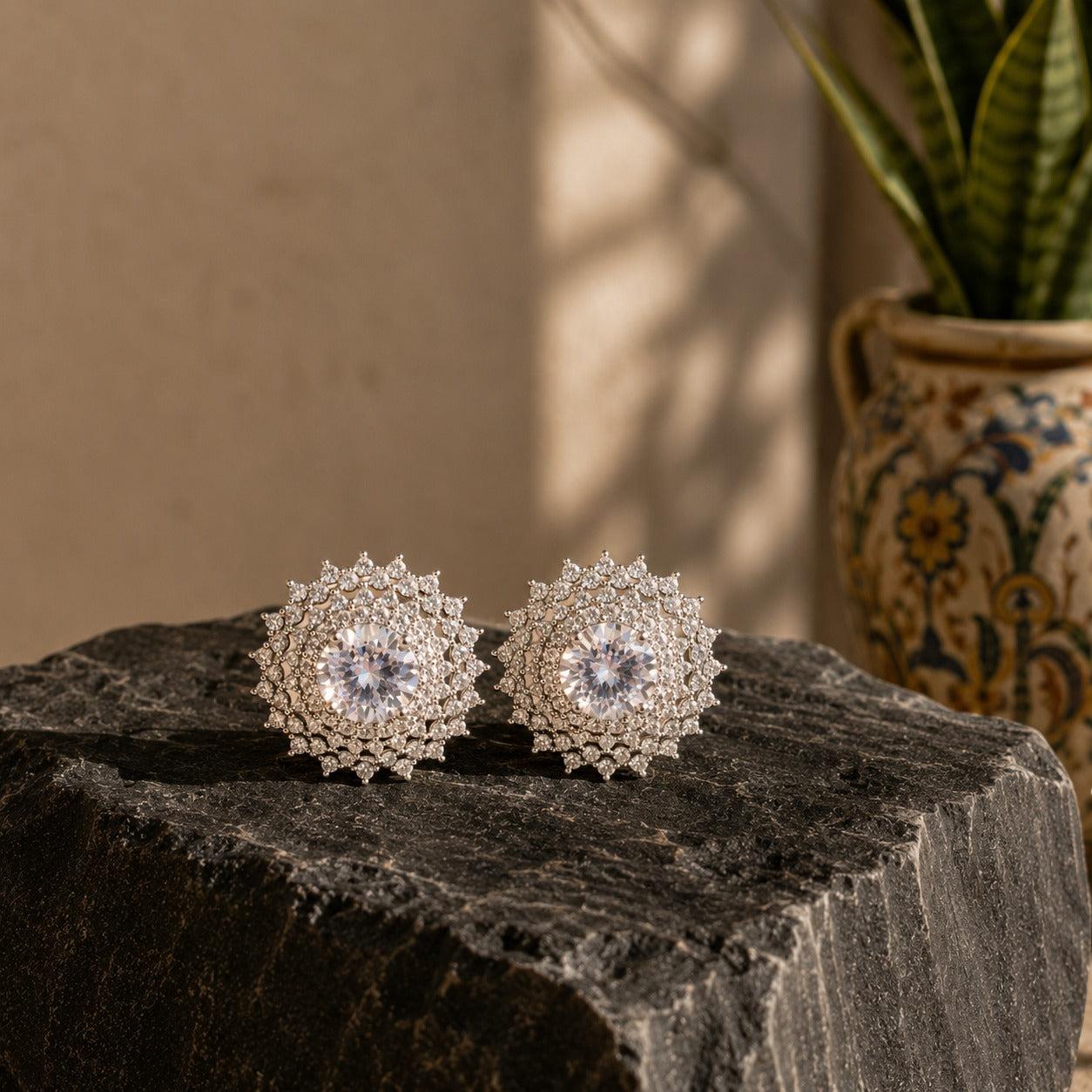 Silver radiant halo crystal stud earrings featuring brilliant round-cut center stones surrounded by intricate pavé crystal halos, displayed on a premium black natural stone surface.