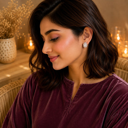 Woman wearing silver teardrop stud earrings with a pearlescent white pear-cut centre stone and pavé halo in a warm luxury indoor setting