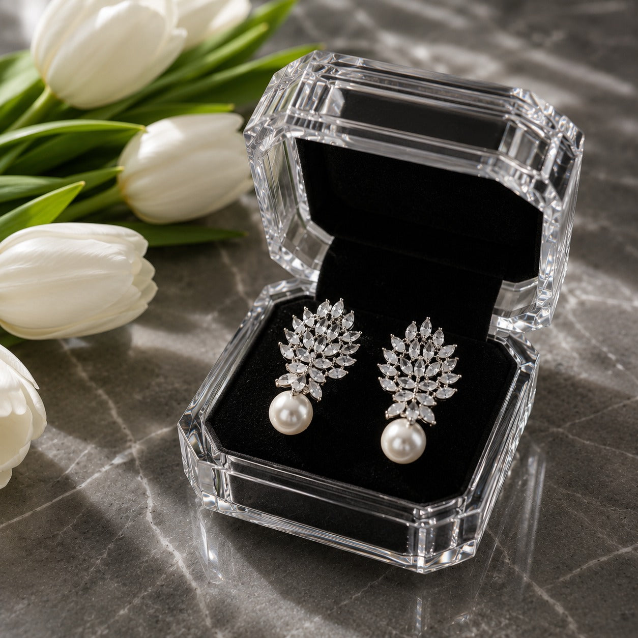 Silver marquise crystal and pearl drop earrings displayed inside a premium crystal jewellery box with black velvet interior beside white tulips.