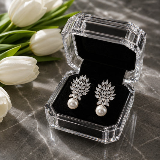 Silver marquise crystal and pearl drop earrings displayed inside a premium crystal jewellery box with black velvet interior beside white tulips.