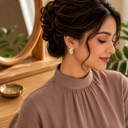 Model wearing gold leaf-inspired crystal stud earrings with a sparkling round-cut stone in a soft side-profile portrait.
