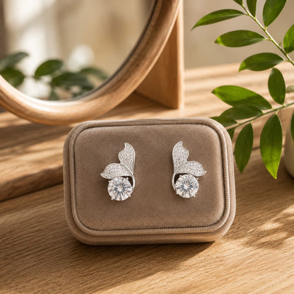 Silver leaf-inspired crystal stud earrings with a round-cut center stone displayed in a soft beige velvet jewellery box.