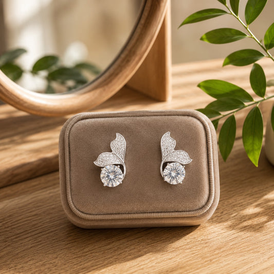 Silver leaf-inspired crystal stud earrings with a round-cut center stone displayed in a soft beige velvet jewellery box.