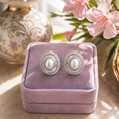Silver oval pearl statement stud earrings with baguette and pavé crystal halo displayed on a lavender velvet jewellery box.