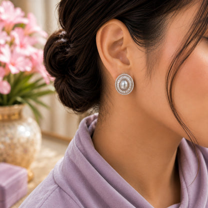 Model wearing silver oval pearl statement stud earrings with a sparkling crystal halo in a soft side-profile portrait