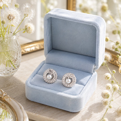 Silver pearl swirl stud earrings with baguette crystal detailing displayed in a soft powder blue velvet jewellery box.