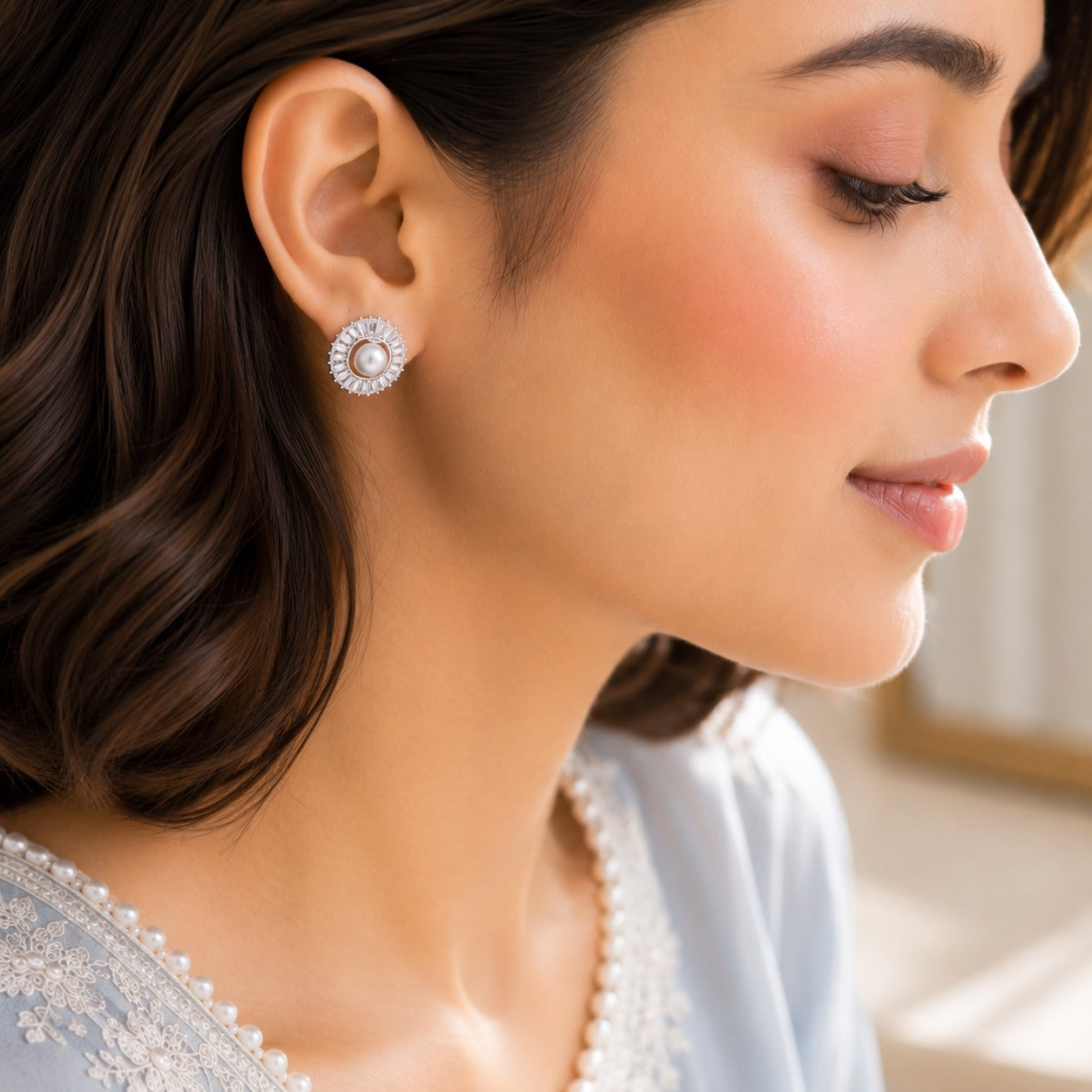 Model wearing silver pearl swirl stud earrings in a soft side-profile portrait with a powder blue embroidered outfit.