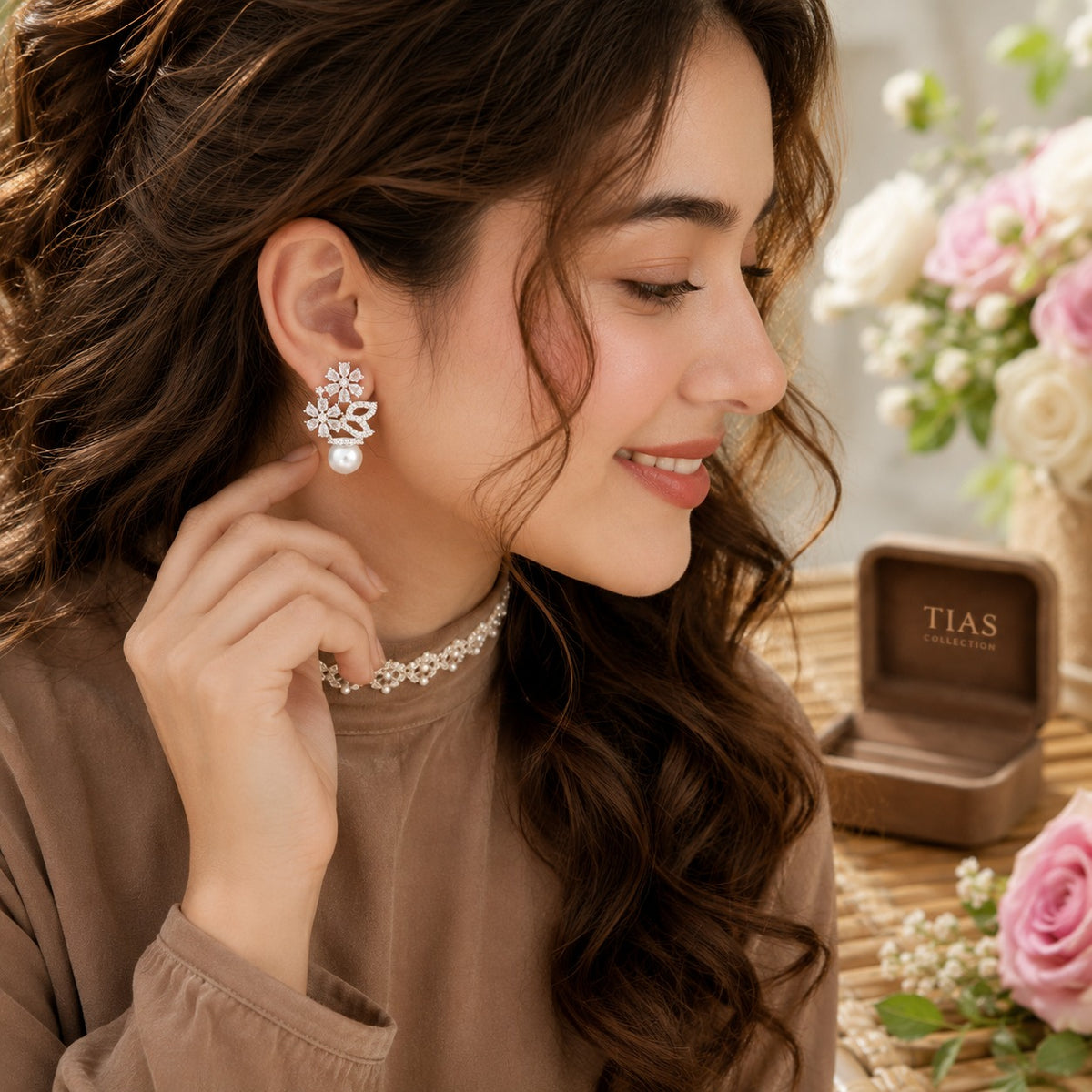 Model wearing silver floral pearl drop earrings with crystal blossoms and a pearl accent in a soft side-profile portrait.
