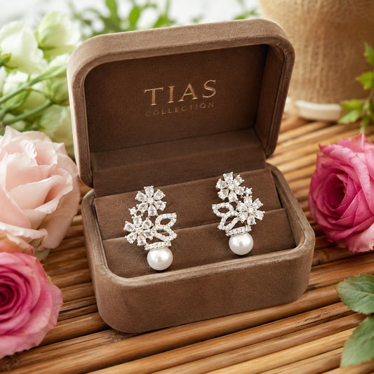 Silver floral pearl drop earrings with crystal flower clusters and pavé leaf details displayed in a mocha velvet jewellery box.
