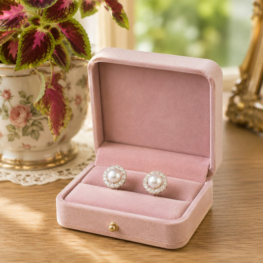 Round gold-tone pearl halo stud earrings with crystal detailing displayed in a soft blush pink velvet jewellery box.