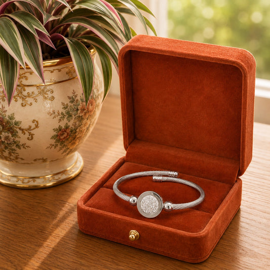 Silver twisted cable bracelets with a crystal pavé circular centerpiece displayed inside a burnt terracotta velvet jewellery box on a wooden table beside a decorative indoor plant.