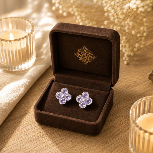 Silver floral stud earrings with lavender crystals in a four-petal clover design displayed in a mocha velvet jewellery box.