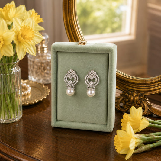 Silver pearl drop earrings with floral crystal accents and an open halo design displayed on a sage green velvet jewellery stand.