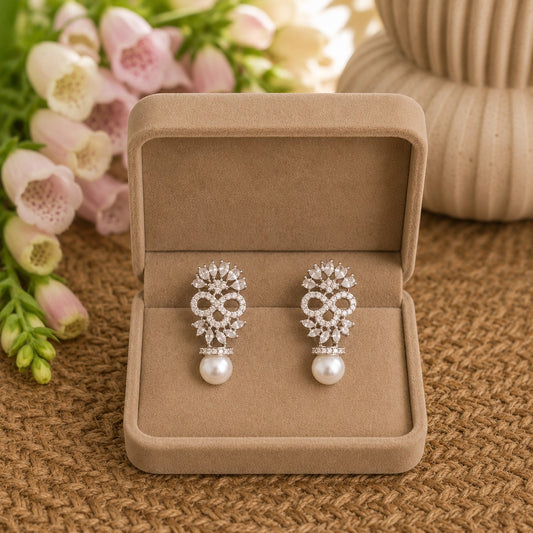 Silver pearl drop earrings with marquise-cut crystals and intricate openwork detailing displayed in a soft beige velvet jewellery box.
