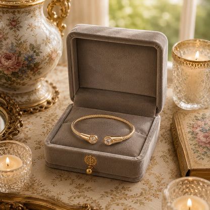 Gold twisted cable cuff bracelet displayed inside a premium grey velvet jewellery box with decorative candlelight setting