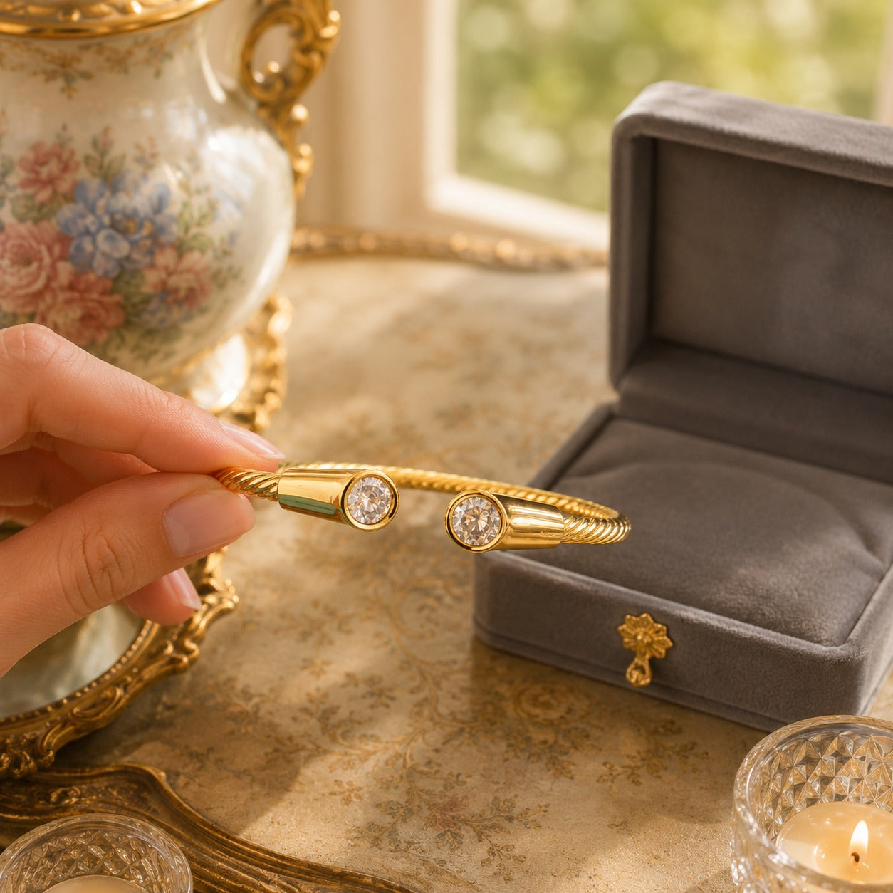 Gold twisted cable cuff bracelet with bezel-set crystals held beside a grey velvet jewellery box
