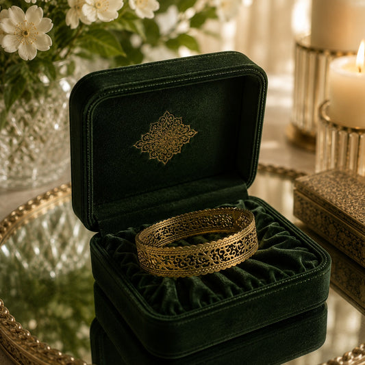 Gold filigree cuff bracelet displayed in a deep green velvet jewellery box with floral accents