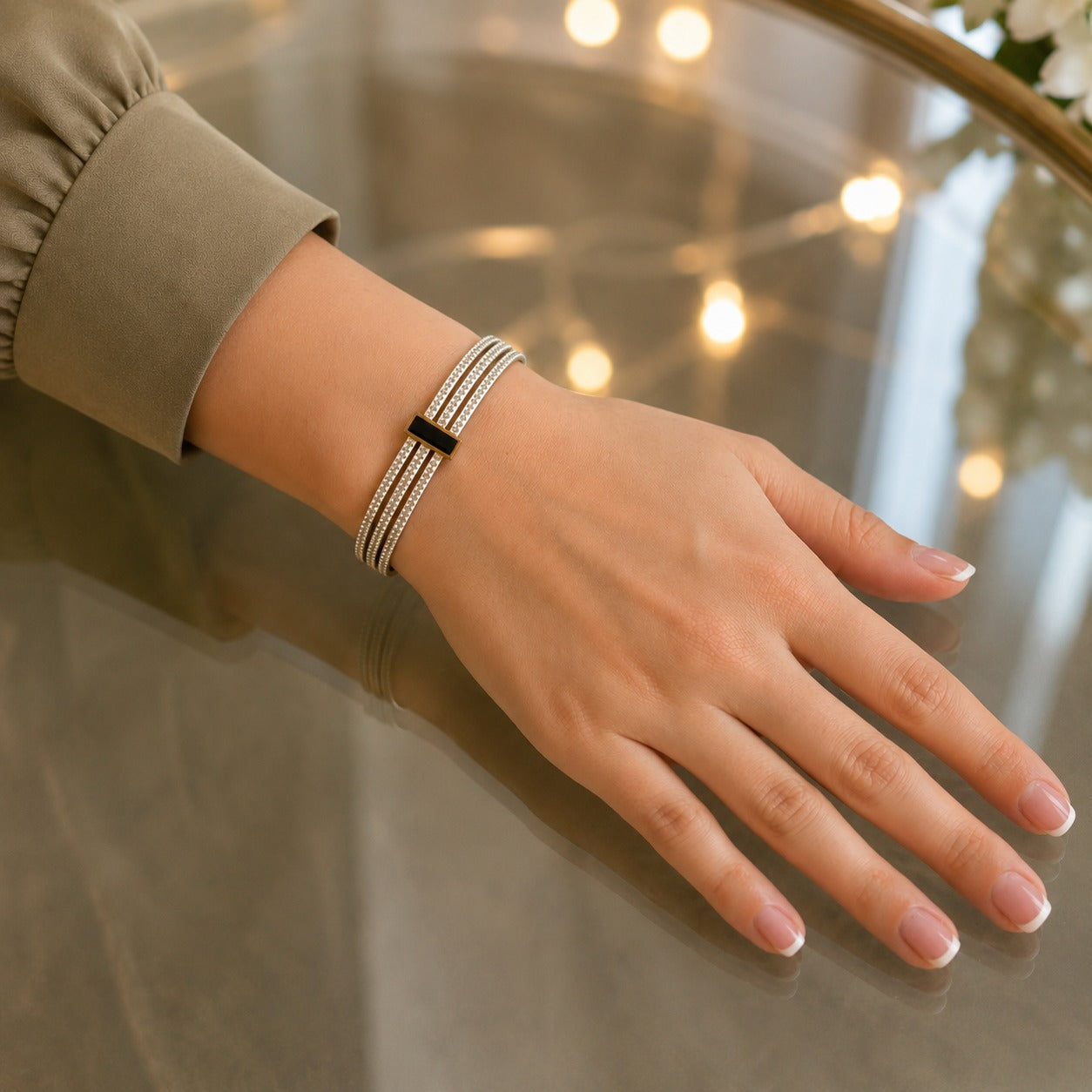 A close-up of a woman's hand and wrist wearing a slim metallic bracelet with a central black rectangular accent,