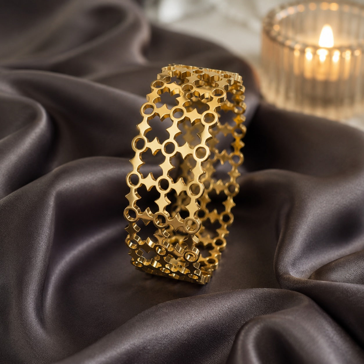 Gold geometric openwork cuff bracelet displayed on black satin with soft candlelight