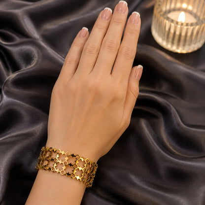Gold openwork cuff bracelet worn on the wrist against a black satin backdrop