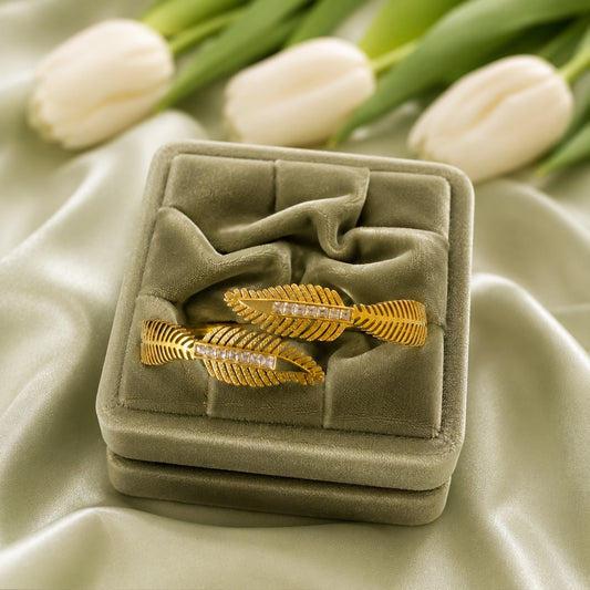 Gold feather bracelet with crystal detailing displayed on a premium sage velvet jewellery cushion with white tulips