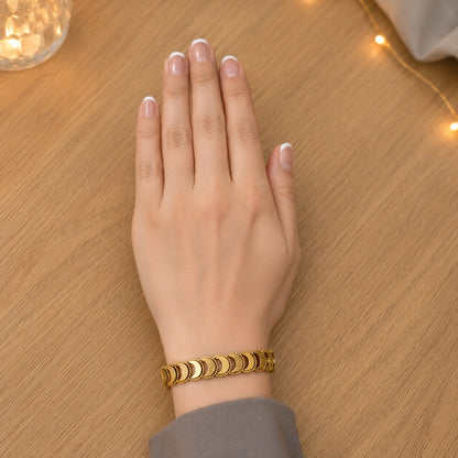 Gold crescent link bracelet worn on the wrist on a natural wood surface