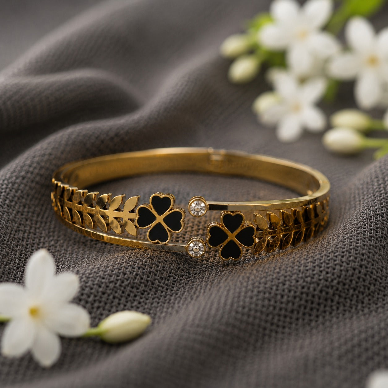 Black clover front-open magnetic bracelet on charcoal grey fabric with jasmine flowers.