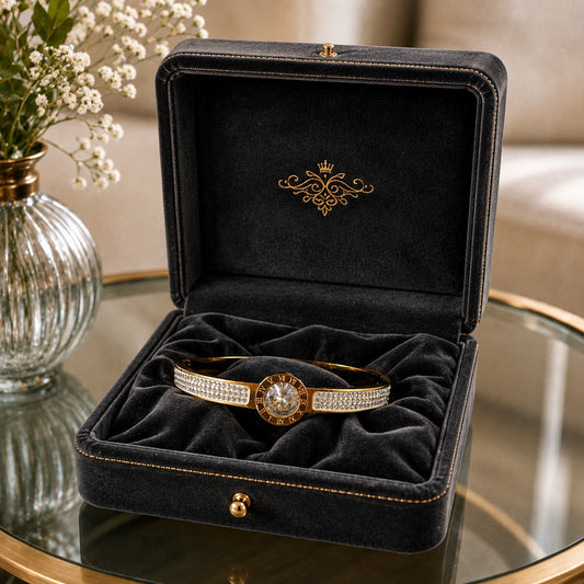 Gold crystal bracelet displayed inside a premium black velvet jewelry box with luxurious folds on a glass tabletop beside white flowers.