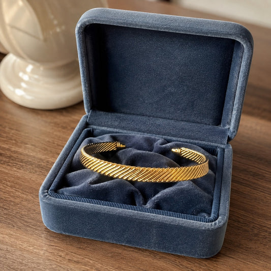 Gold twisted cable cuff bracelet resting naturally inside a premium blue velvet jewelry box with a soft luxury background.