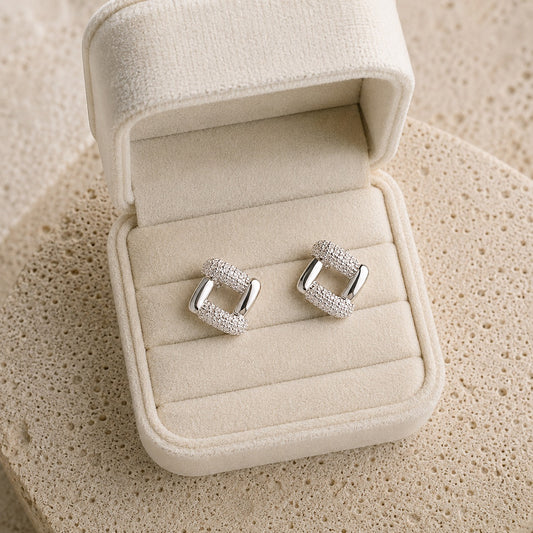 Silver geometric pavé stud earrings displayed in a premium ivory velvet jewelry box on a natural travertine surface