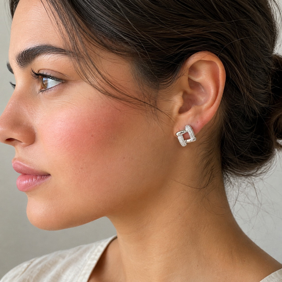Woman wearing silver pavé geometric link stud earrings in a side-profile portrait