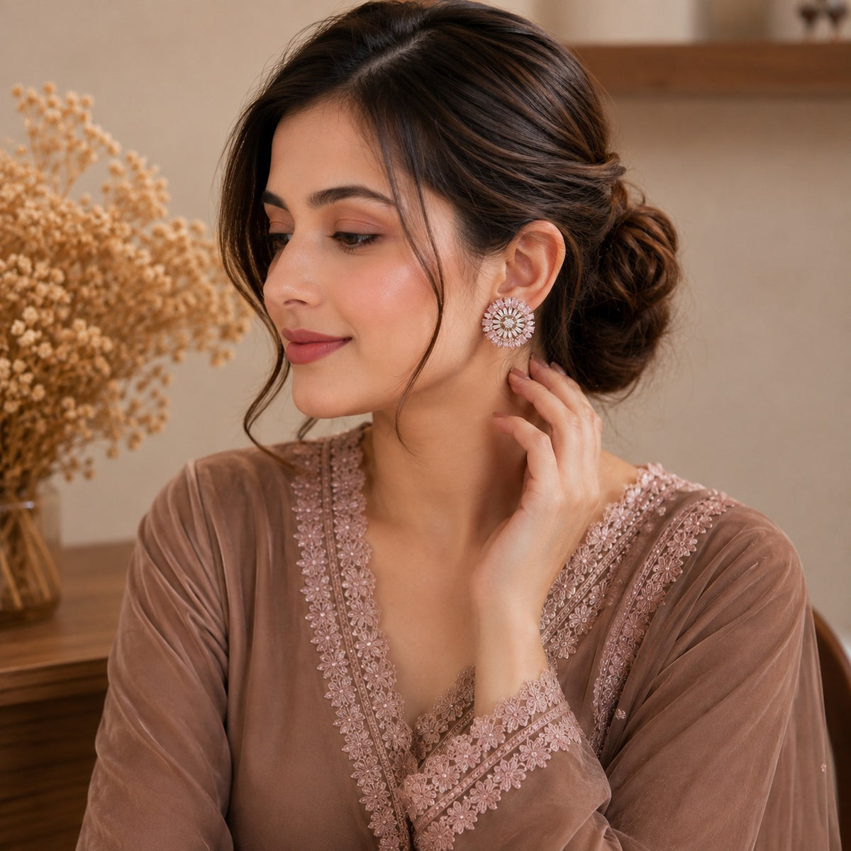 Model wearing rosé floral stud earrings with a soft updo hairstyle and coordinated formal outfit in a warm indoor setting.