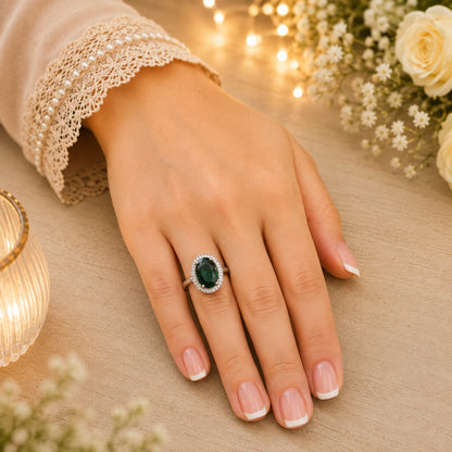 
Deep green oval halo ring worn on a hand with French manicure in a warm luxury lifestyle setting.