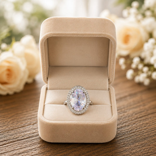 Silver oval halo ring displayed inside an ivory velvet jewellery box with soft floral décor.