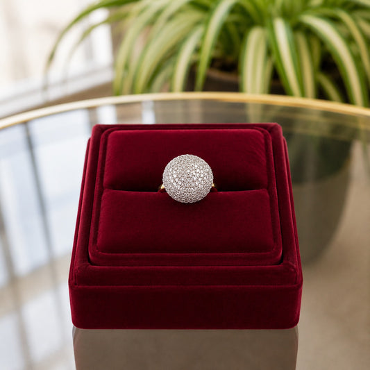 Front view of a pavé dome statement ring presented on a premium burgundy velvet ring stand with natural daylight and greenery in the background.