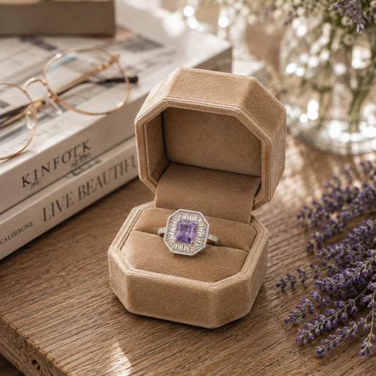 S925 sterling silver octagonal halo ring with baguette zircon accents and purple gem displayed inside a premium beige velvet octagonal ring box on a rustic wooden table with lavender, books, and soft ambient lighting.