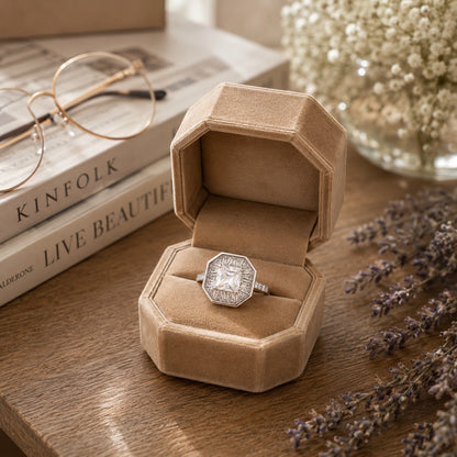S925 sterling silver octagonal halo ring with baguette zircon accents and clear gem displayed inside a premium beige velvet octagonal ring box on a rustic wooden table with lavender, books, and soft ambient lighting.
