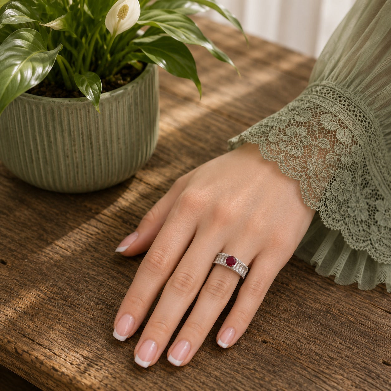 Model wearing an S925 sterling silver ring featuring a ruby-red center stone with baguette zircon detailing, photographed on a wooden tabletop with a soft green lace sleeve and natural daylight.