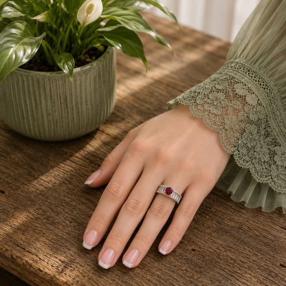 Model wearing an S925 sterling silver ring featuring a ruby-red center stone with baguette zircon detailing, photographed on a wooden tabletop with a soft green lace sleeve and natural daylight.