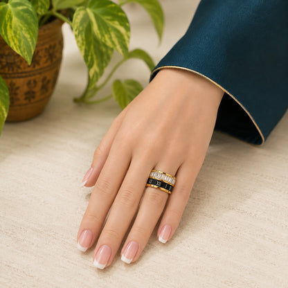 Woman wearing a heavyweight stainless steel Roman numeral band ring with baguette crystal accents on a neutral stone surface beside a green potted plant.