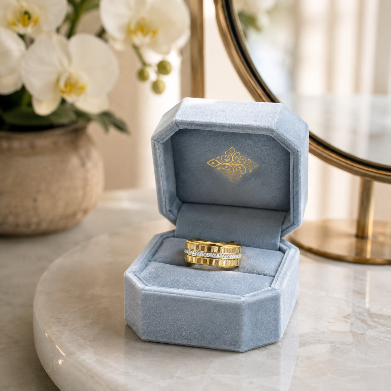 Gold-tone stainless steel ridged band presented inside a premium powder blue velvet jewelry box with a softly blurred luxury vanity background.