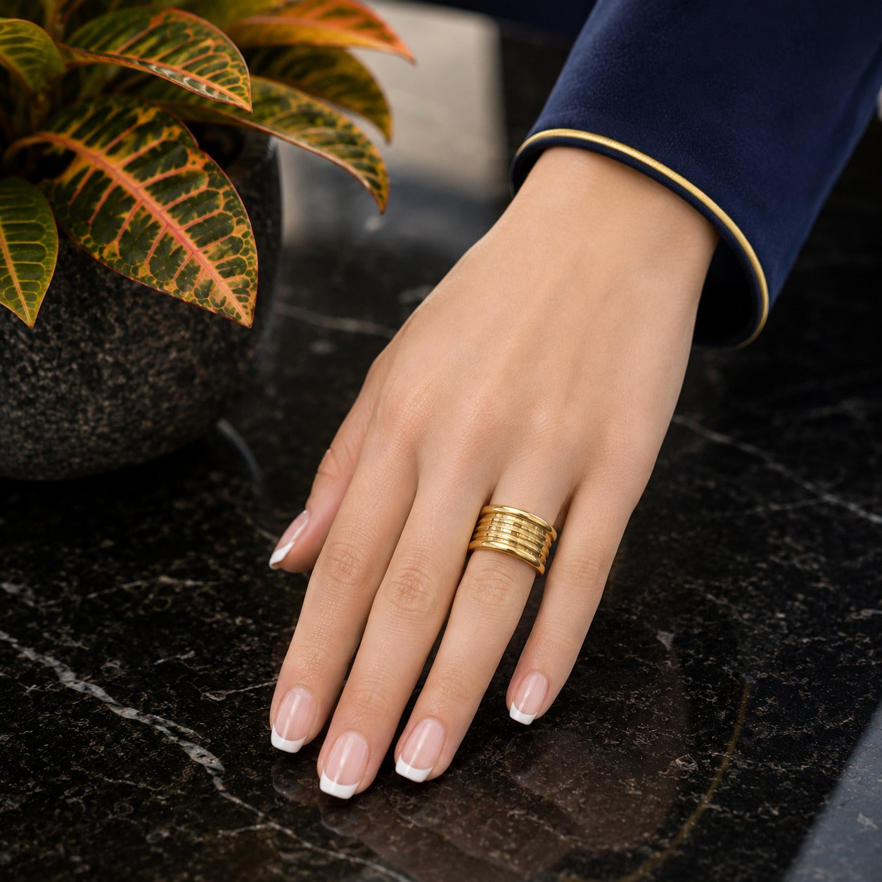 Heavy gold-tone stainless steel band ring worn on a hand with French manicure on a black marble surface.