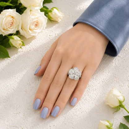 Floral crystal statement ring worn on a hand with soft blue manicure and white rose background.