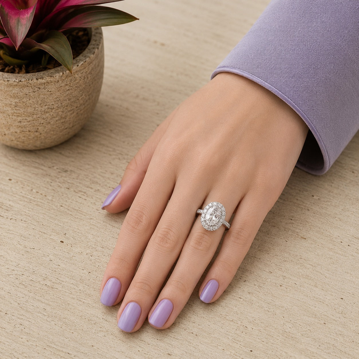 Close-up of the crystal clear oval halo ring worn on the finger, highlighting the pavé halo and polished stainless steel band.